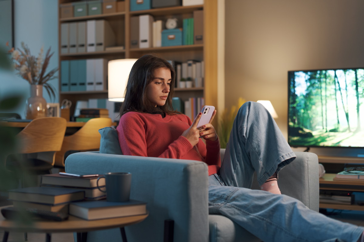Girl relaxing on the armchair and using her smartphone