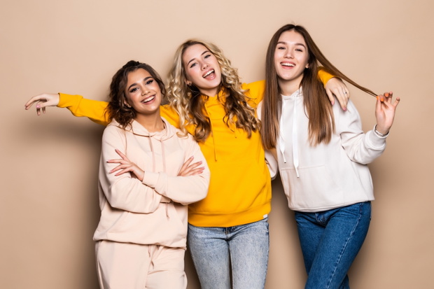 Three women friends standing together on beige background