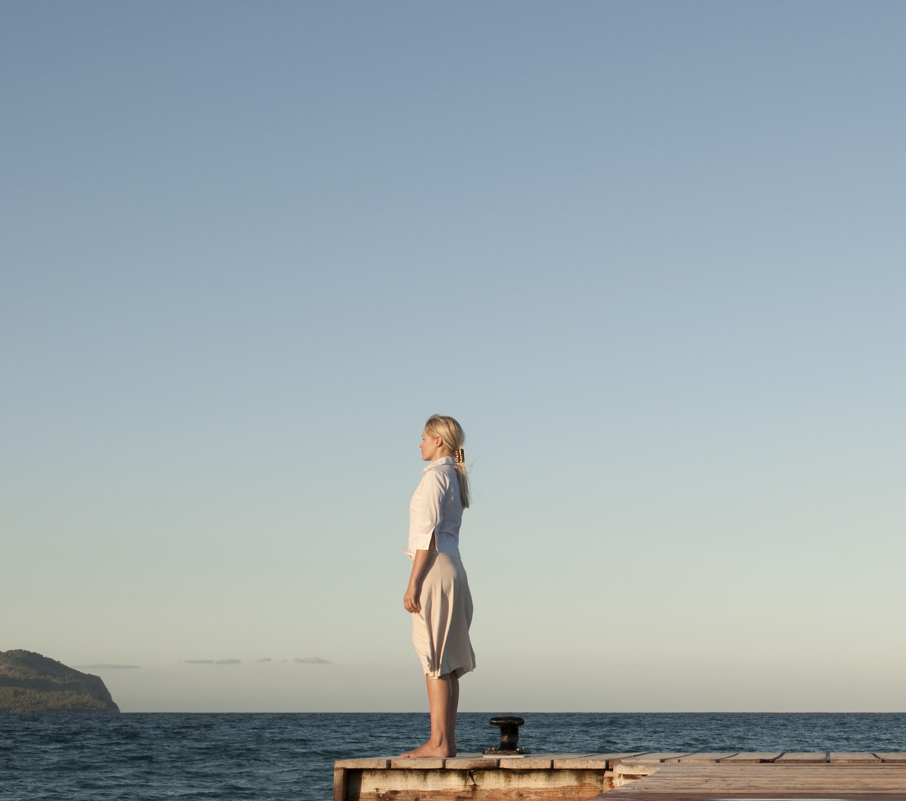 Couple standing back to back on pier, side view