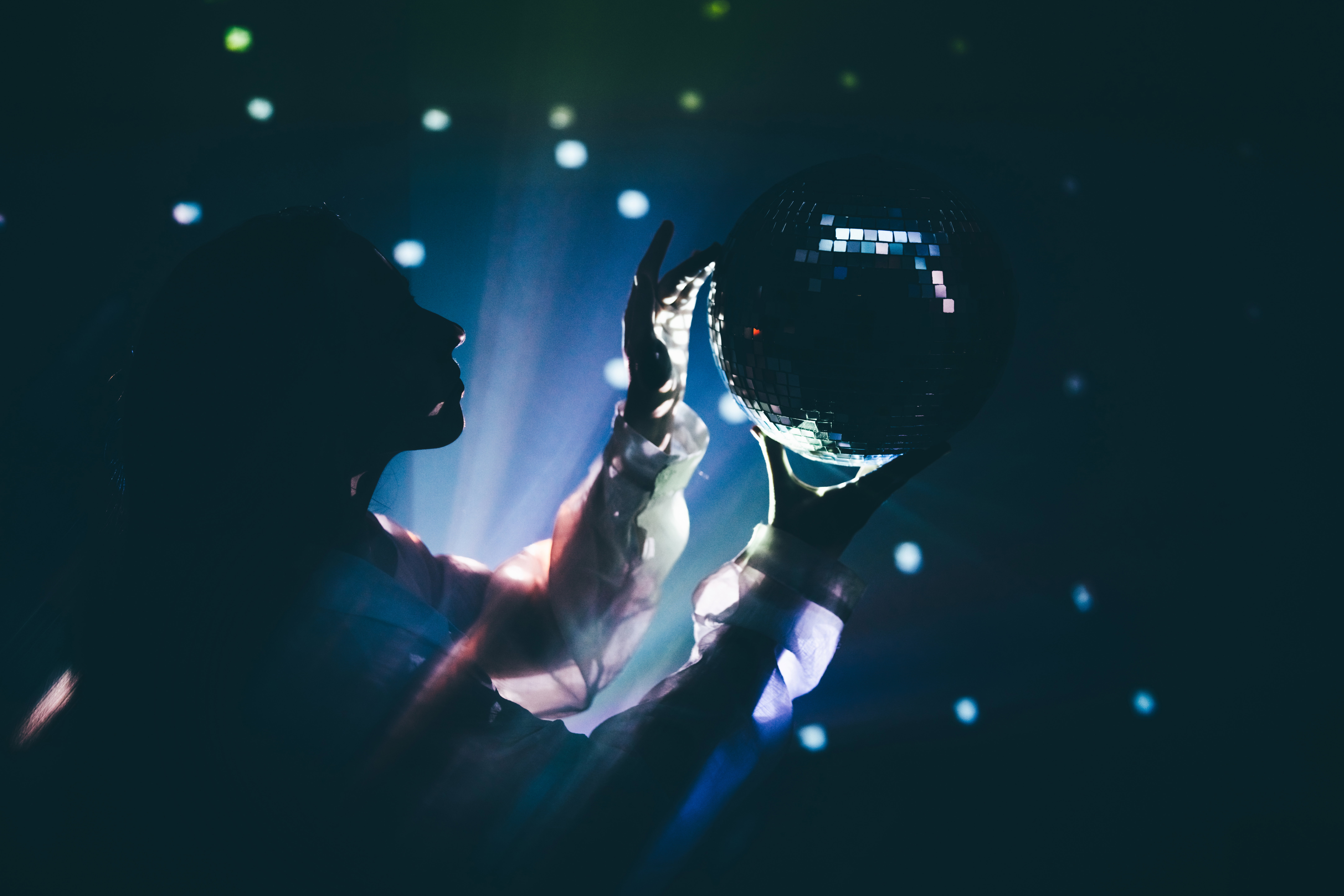 A women is  holding a disco ball that reflects light onto their hands and face in a dark, atmospheric setting. Mystery, magic, and celebration.