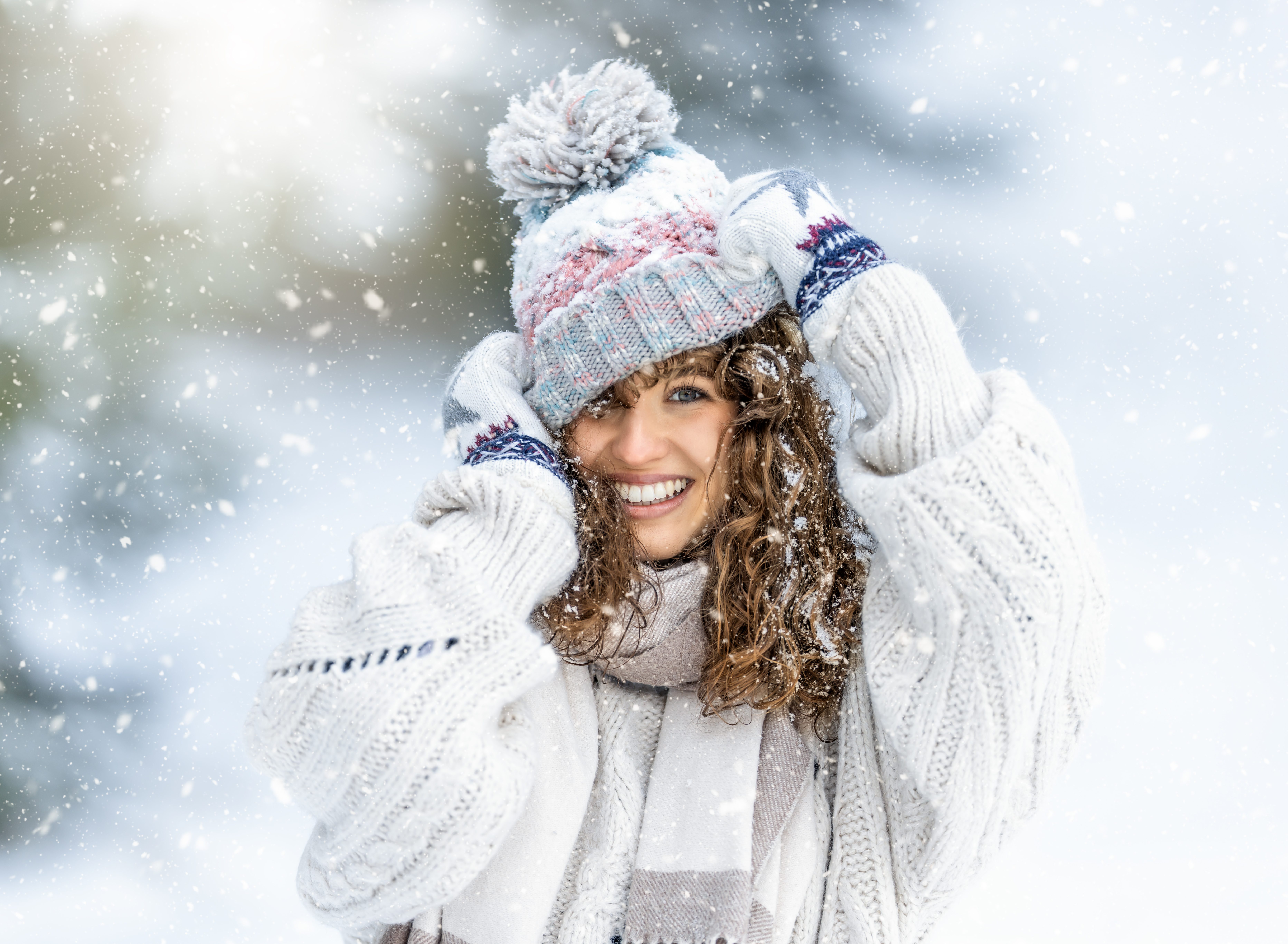 Portrait of a beautiful curly young woman in a knitted sweater, gloves and a hat enjoying winter, snow and snowfall.