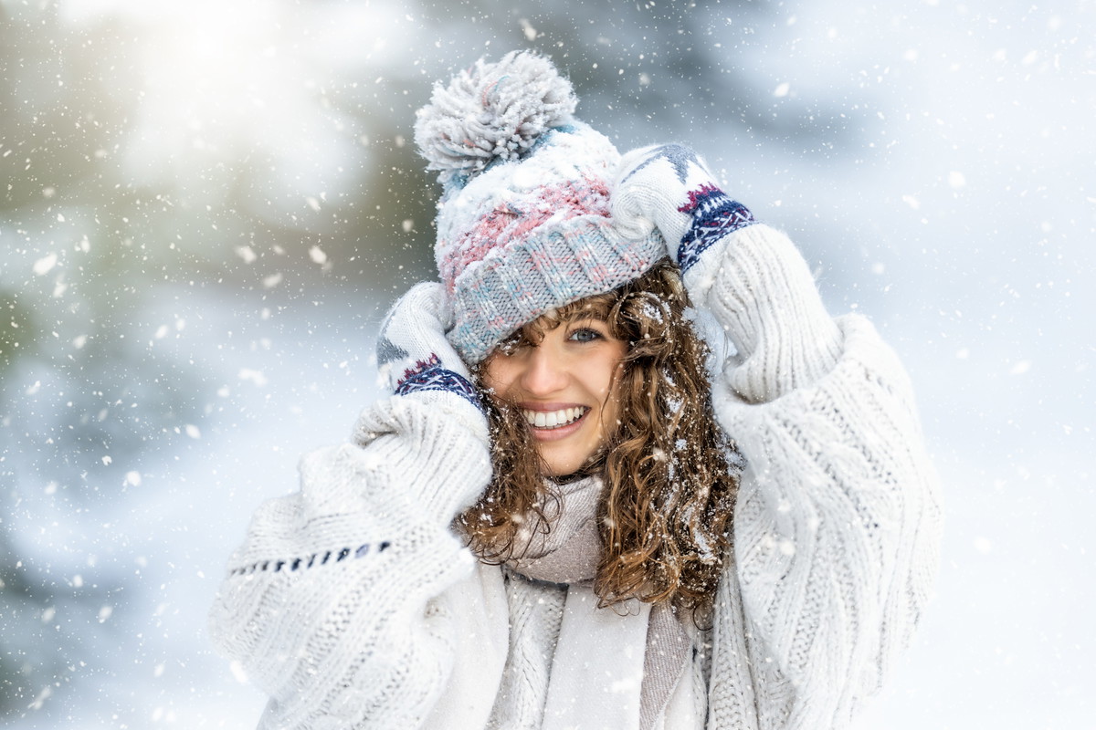 Portrait of a beautiful curly young woman in a knitted sweater, gloves and a hat enjoying winter, snow and snowfall.