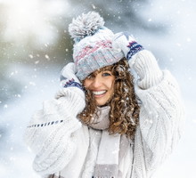 Portrait of a beautiful curly young woman in a knitted sweater, gloves and a hat enjoying winter, snow and snowfall.