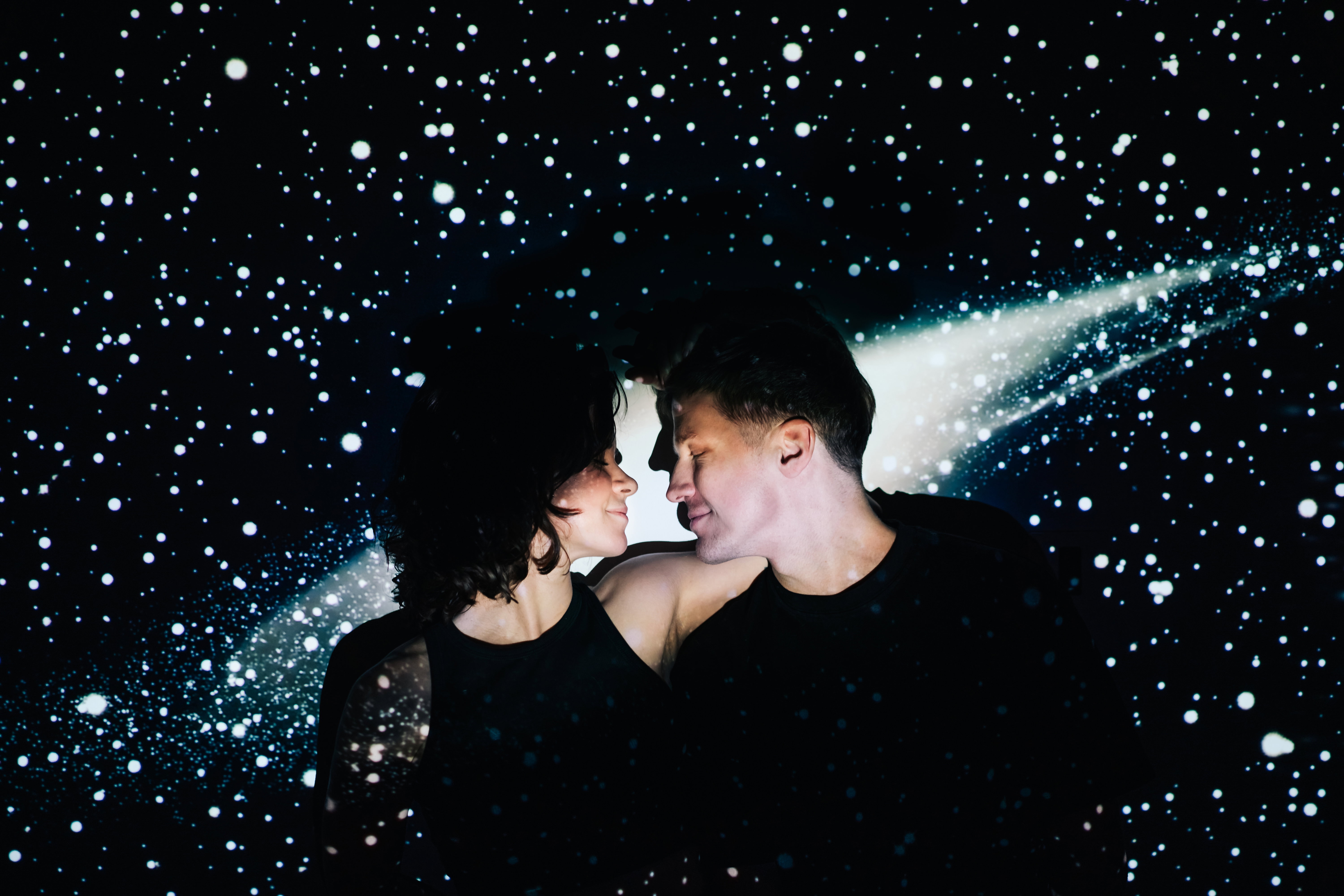 Couple embracing in front of a projected starry sky background, evoking cosmic romance and connection in a dreamy setting.