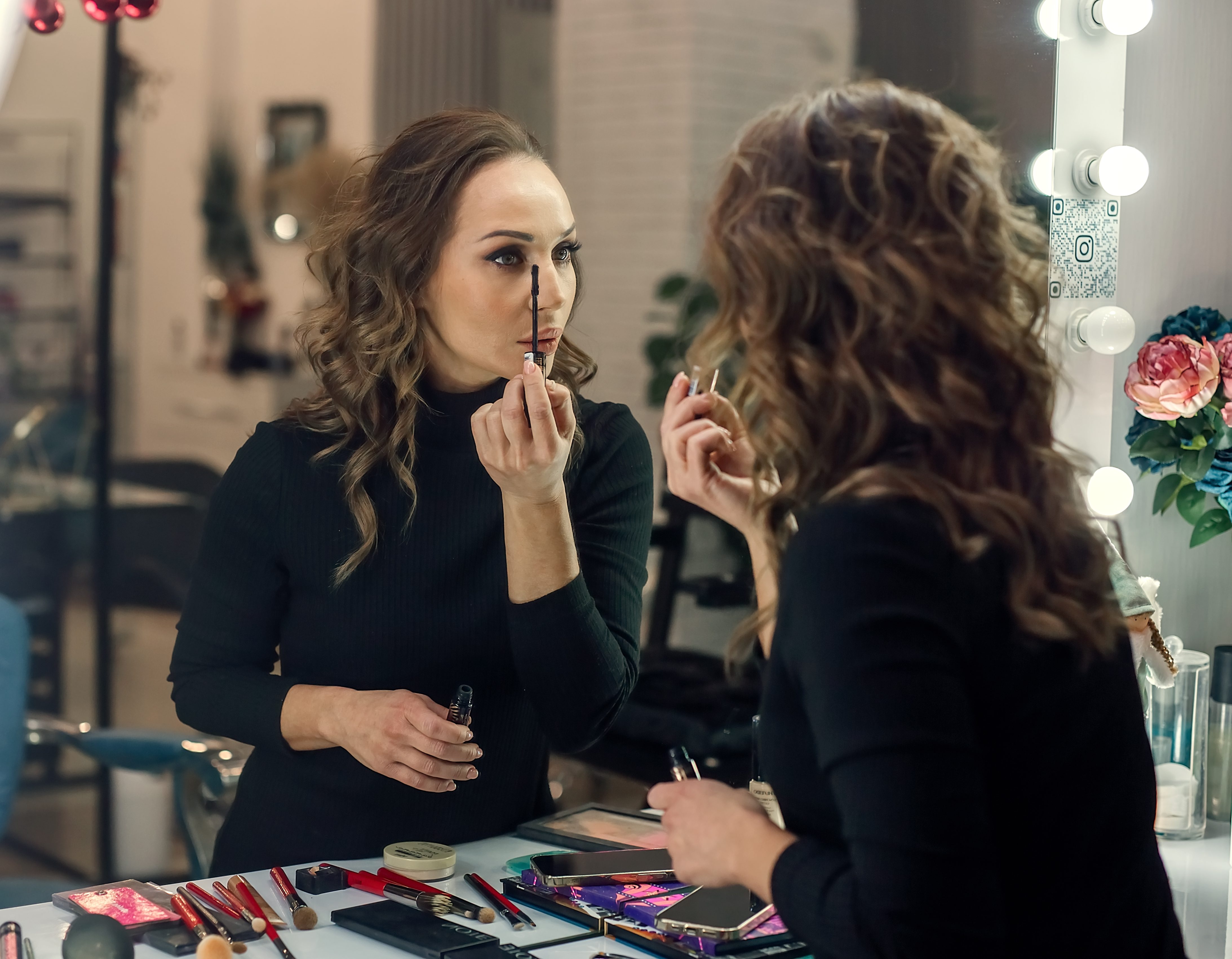 A beautiful young woman applies makeup to herself in the mirror.