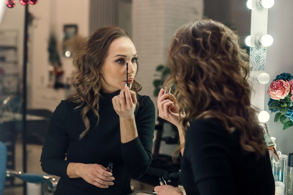 A beautiful young woman applies makeup to herself in the mirror.