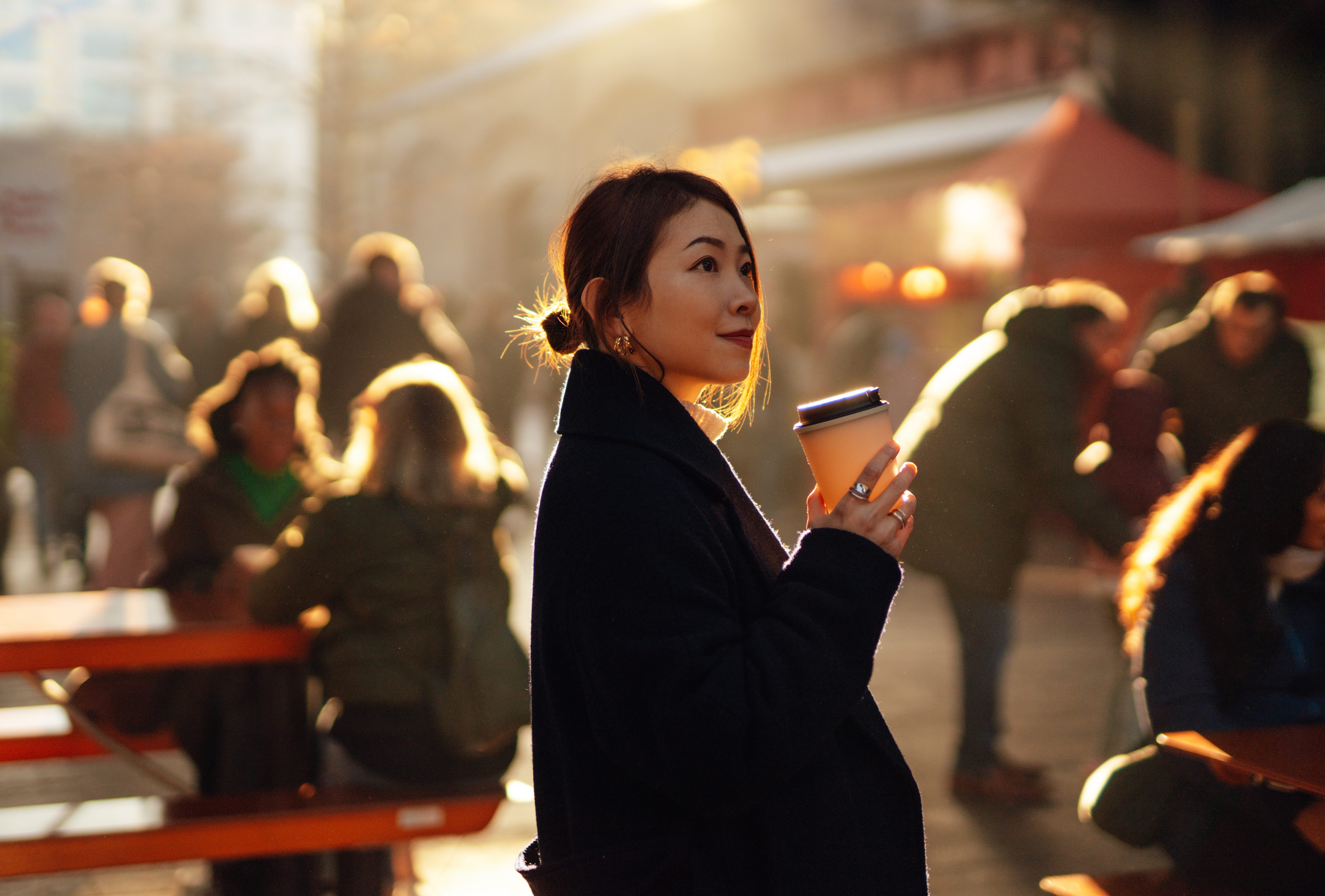 Young Asian woman drinking coffee at local street food market with moody sunlight