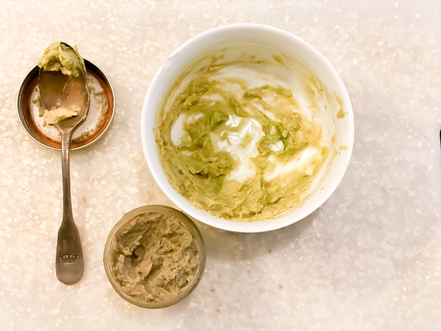 jar of homemade avocado facial scrub paste or beauty mask with silver spoon &amp; white bowl