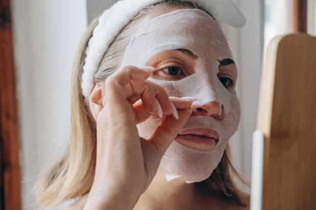 facial skin care woman applies moisturizing facial tissue mask with lifting effect , sheet mask with lifting and anti-age active ingredients