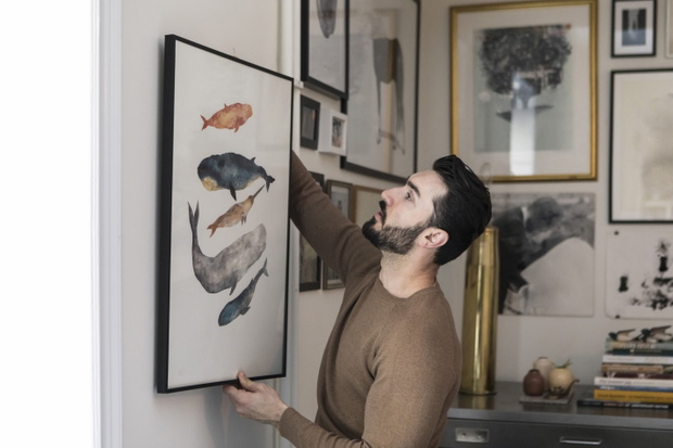 Young man hanging painting on wall at home