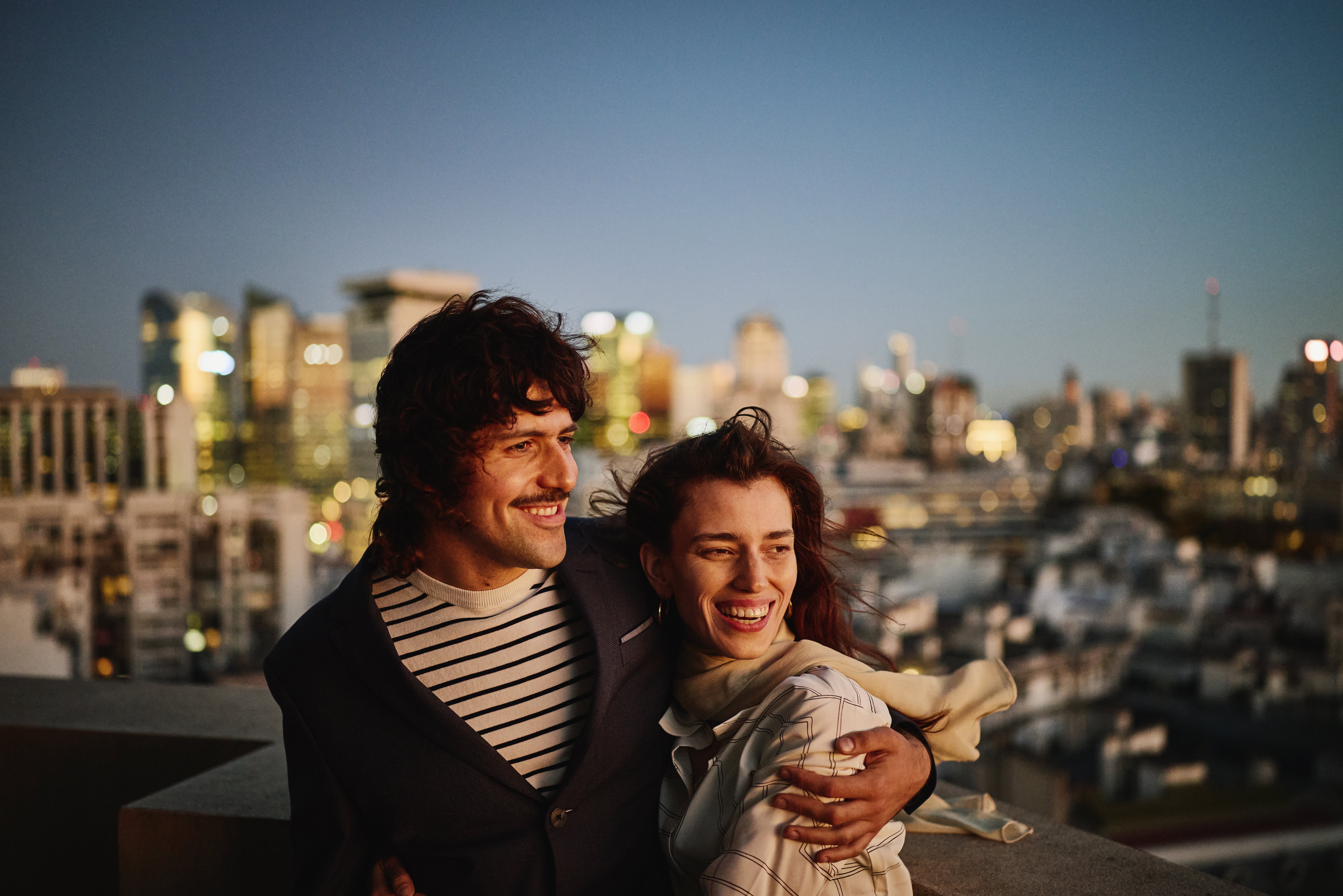 Medium shot smiling couple embracing  on city rooftop at night