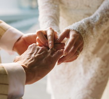 Bride putting ring on groom's finger. Rings exchange. Happy couple celebrating wedding outdoors in summer.