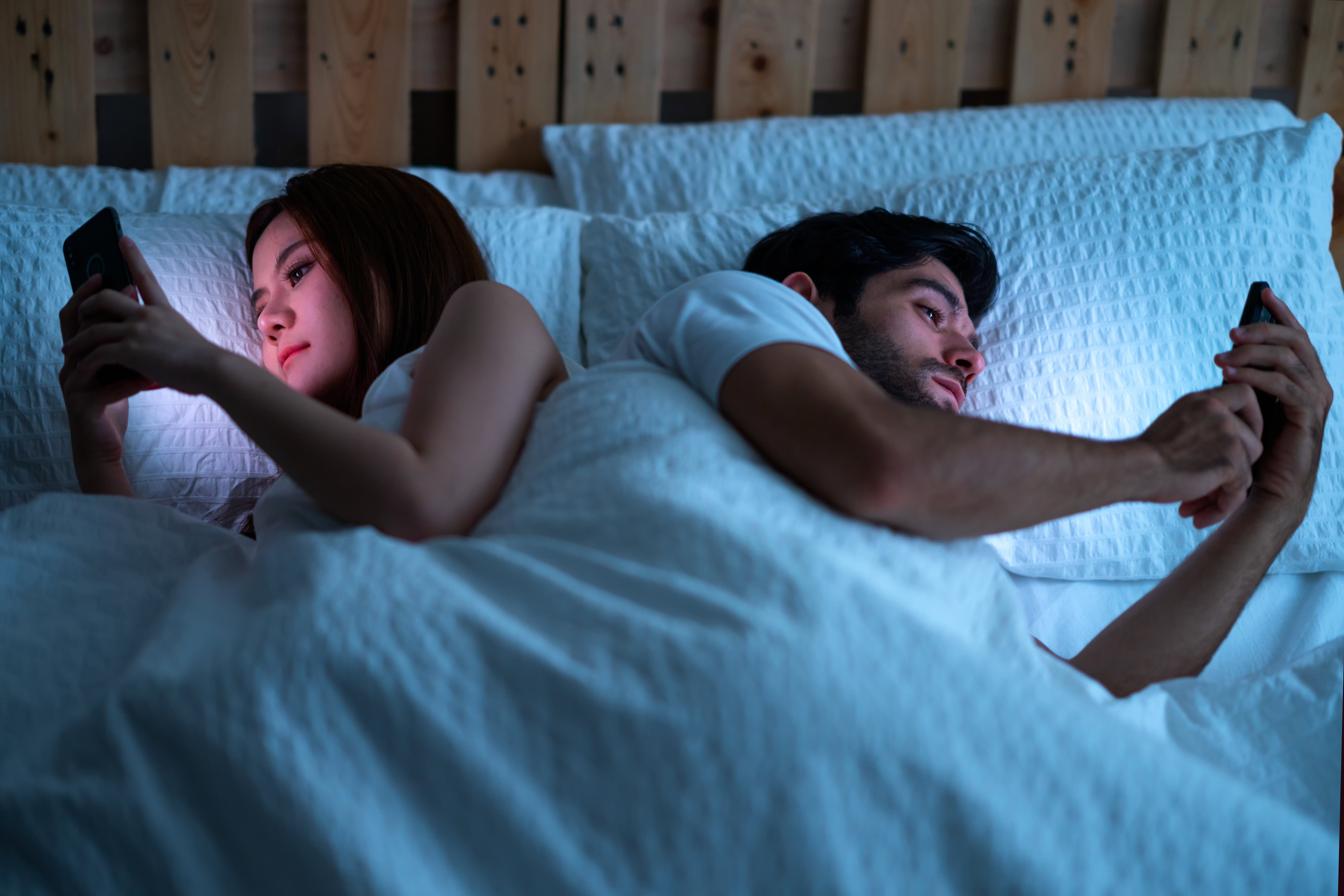 young couple at home in bed late at night using mobile phone in relationship communication problem and internet social media network concept.