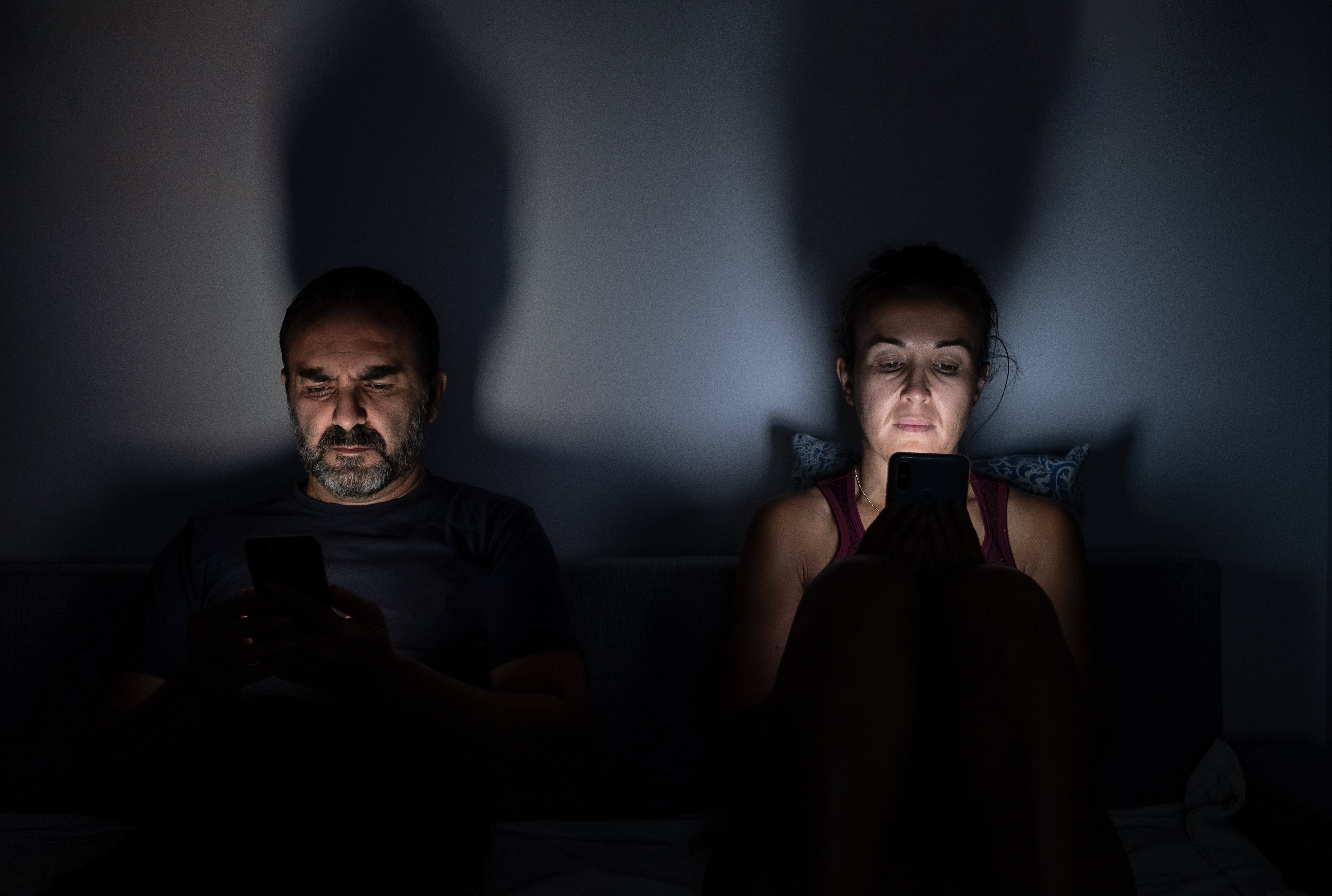 couple using their mobile phones on the sofa at home at night