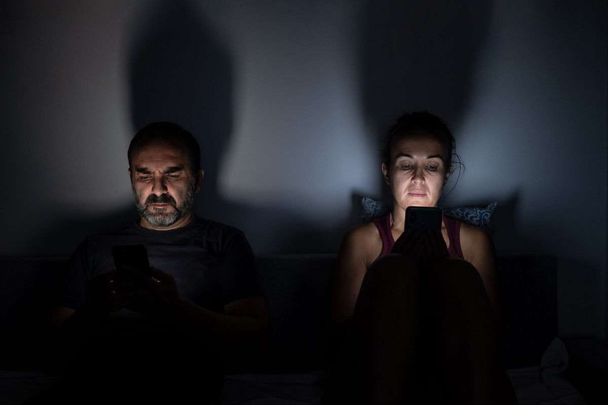 couple using their mobile phones on the sofa at home at night