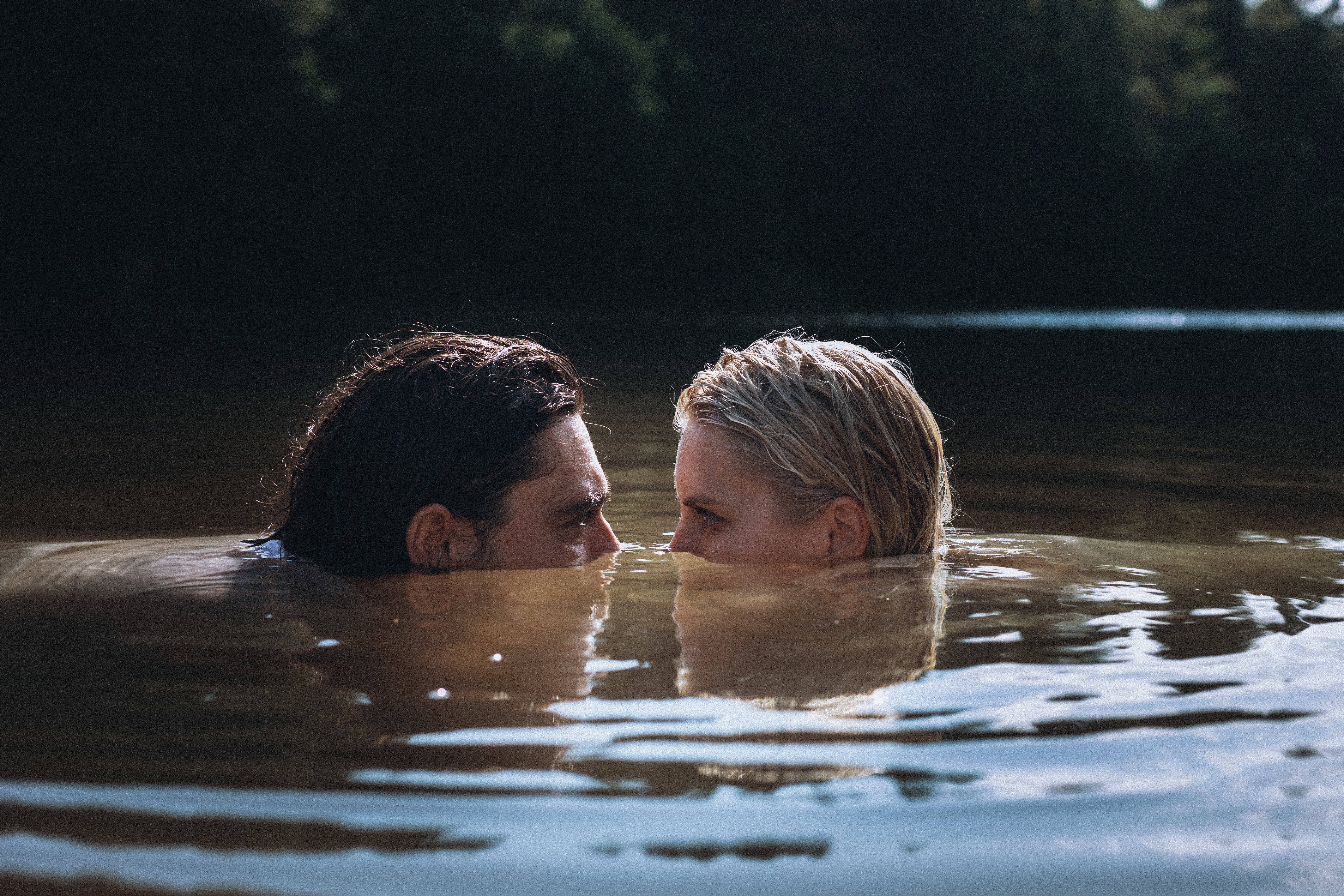 Confident man and delicate woman in problematic relationship swimming in lake, sank under water and looking at each other peeking out of surface with dissatisfied look.