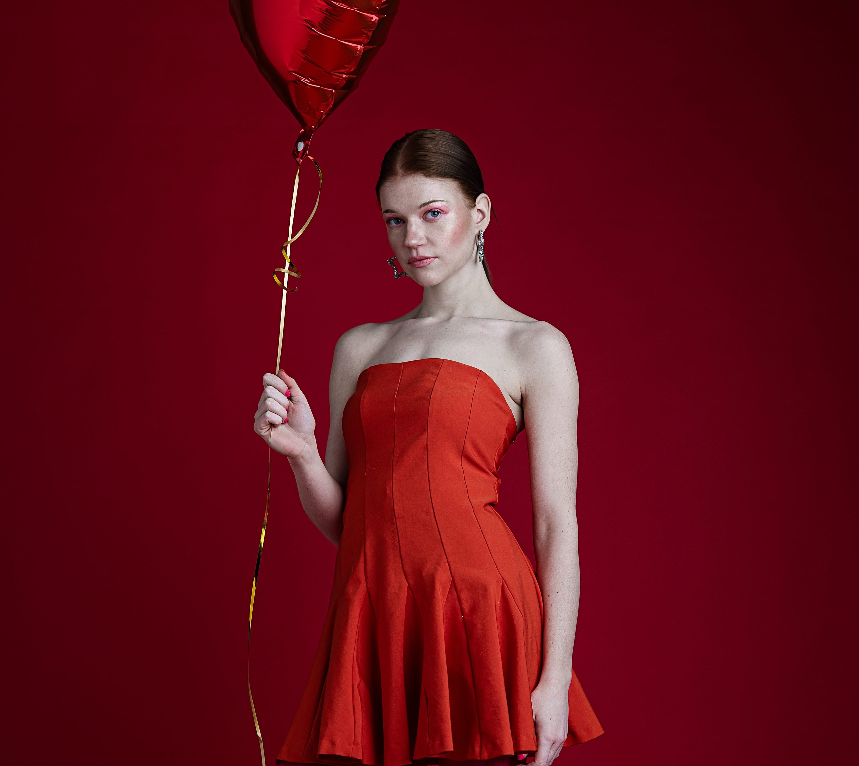 Woman in strapless red dress and pink heart pattern tights holding a heart shape balloon