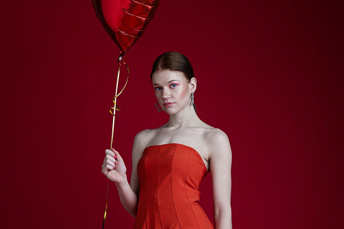 Woman in strapless red dress and pink heart pattern tights holding a heart shape balloon