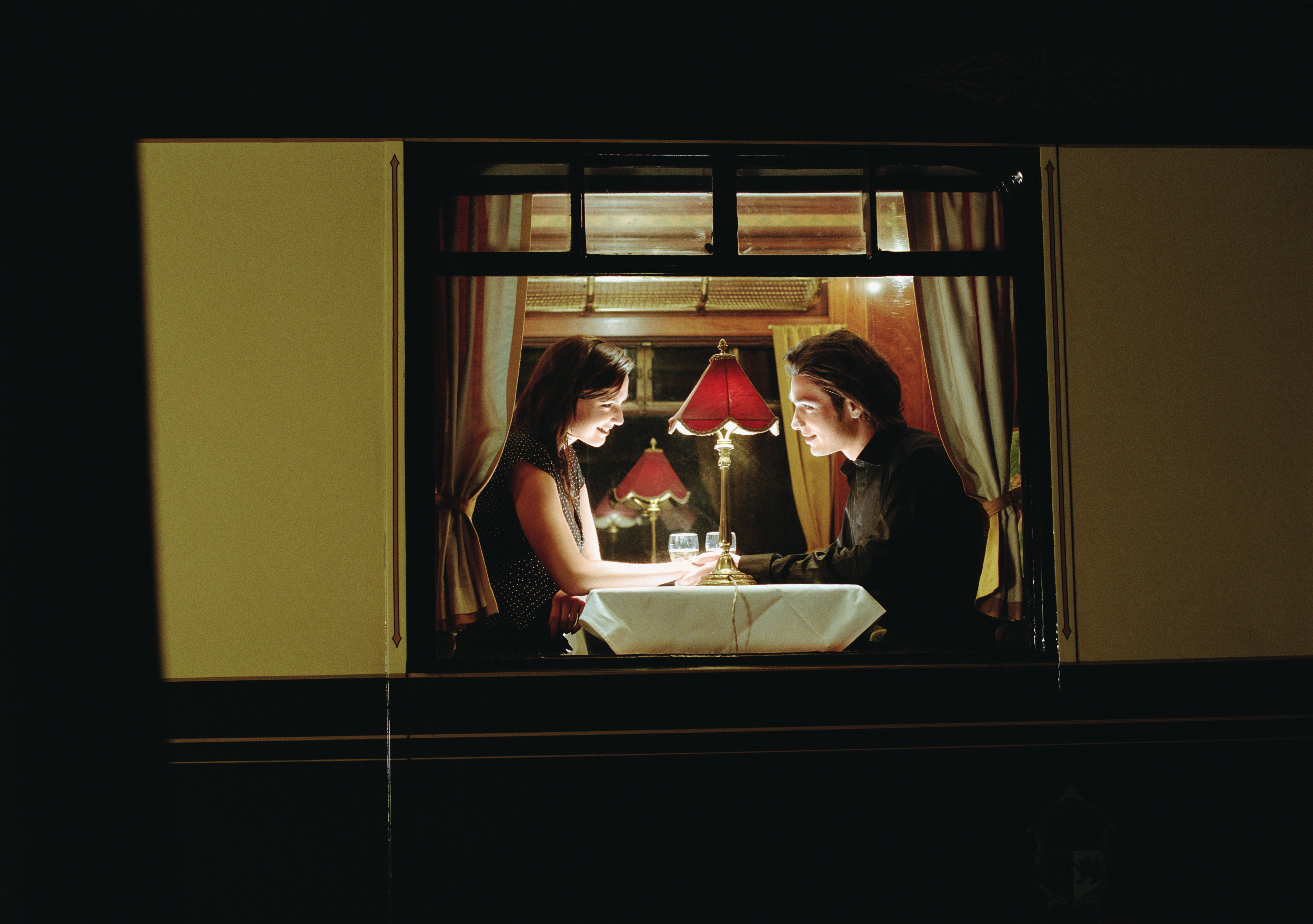 Young couple at table aboard train, exterior view, night