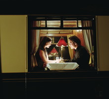 Young couple at table aboard train, exterior view, night