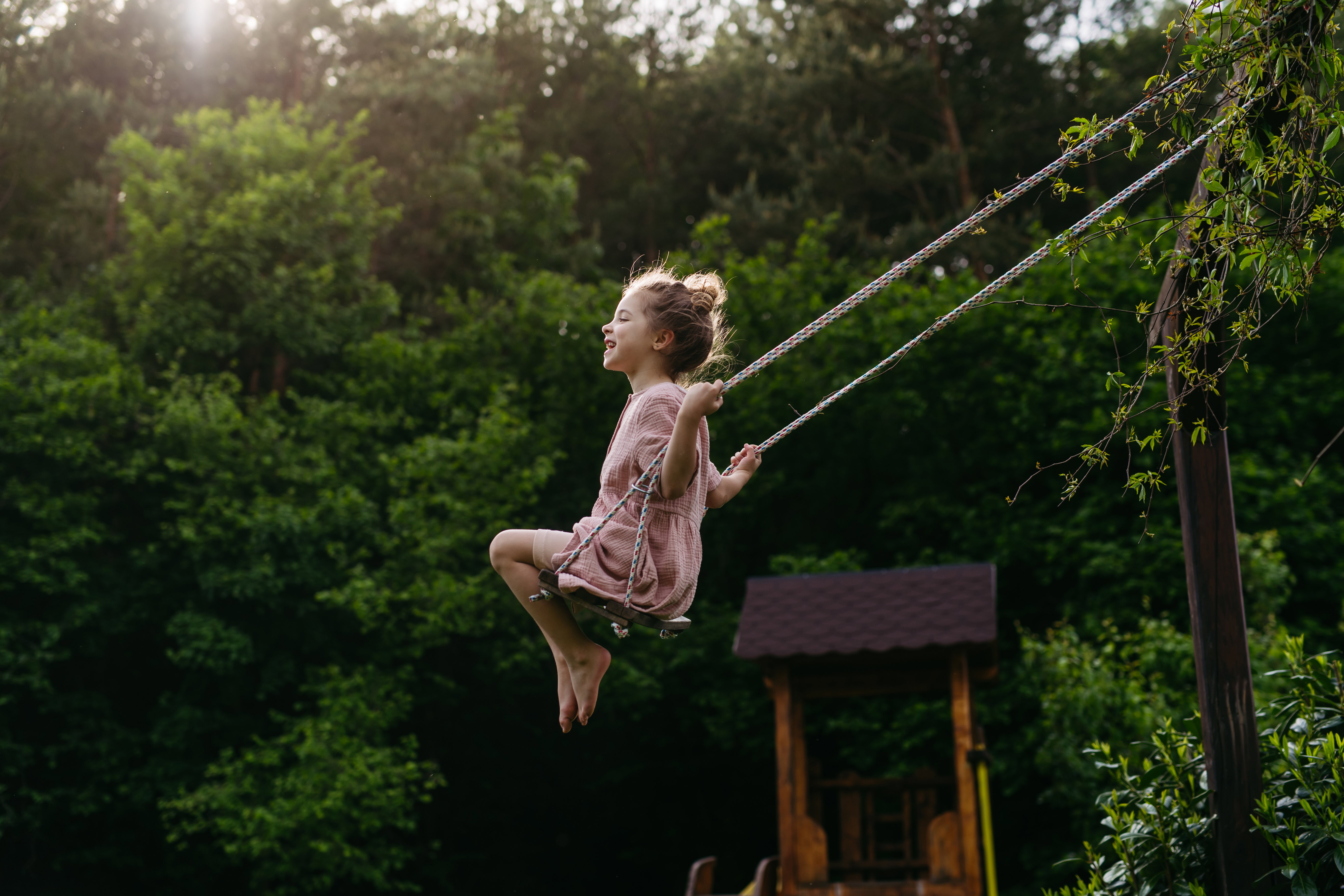 Side view of beautiful girl swinging on garden swing.