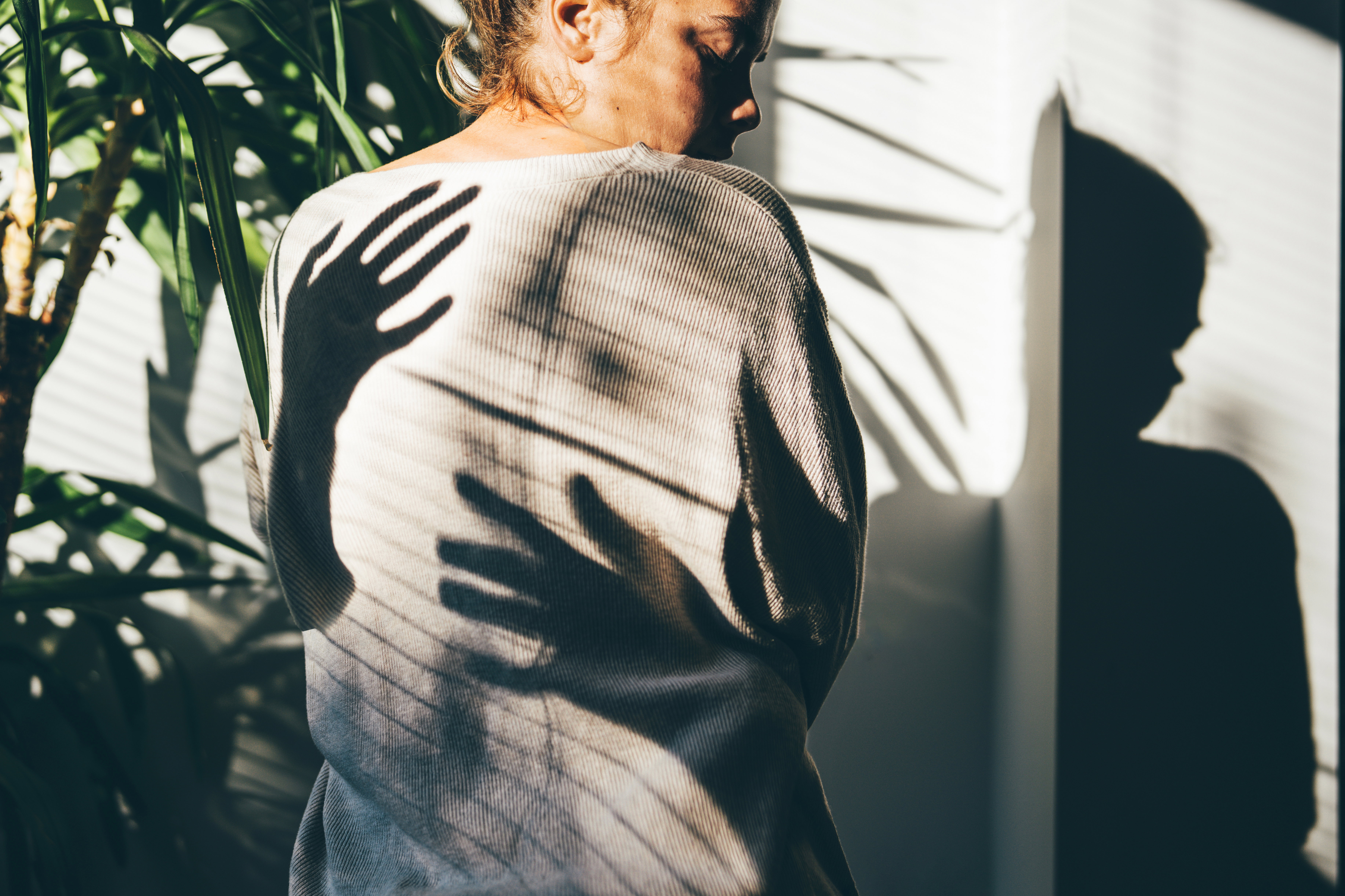 A rear view of a woman, with mysterious shadows cast by her hands in the bright sunlight. This dramatic, high-contrast scene evokes associations with anxiety, fear, mental health issues, and psychological struggle.