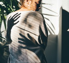 A rear view of a woman, with mysterious shadows cast by her hands in the bright sunlight. This dramatic, high-contrast scene evokes associations with anxiety, fear, mental health issues, and psychological struggle.