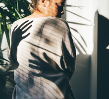 A rear view of a woman, with mysterious shadows cast by her hands in the bright sunlight. This dramatic, high-contrast scene evokes associations with anxiety, fear, mental health issues, and psychological struggle.