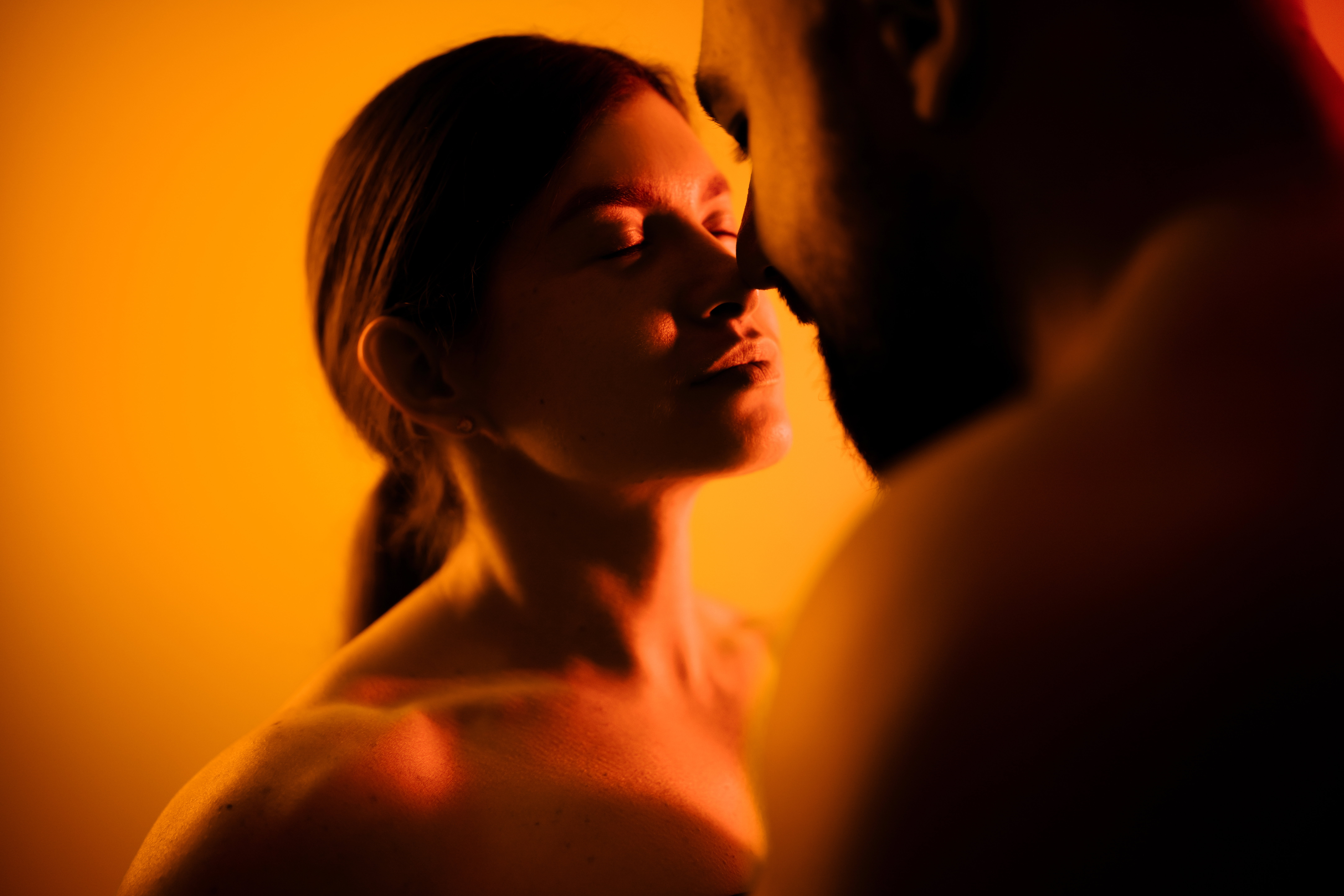 Intimate moment between a couple in warm orange light, close-up kiss anticipation