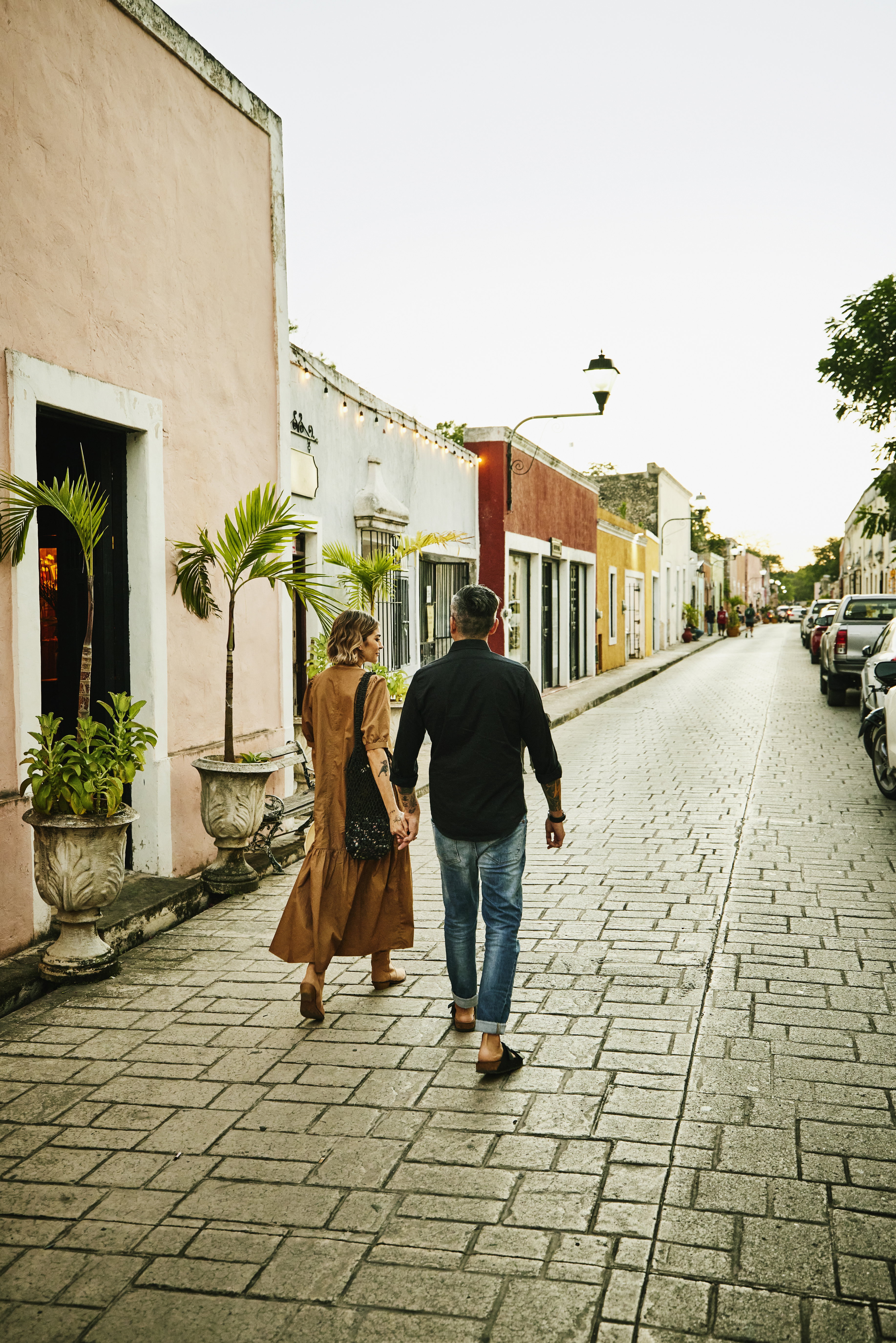 Wide shot rear view of couple holding hands and walking down street while exploring town during vacation