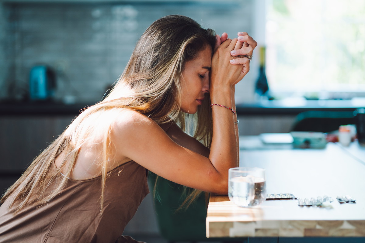 Domestic violence and women mental illness. Crying woman with head in hands drinking pills on the kitchen