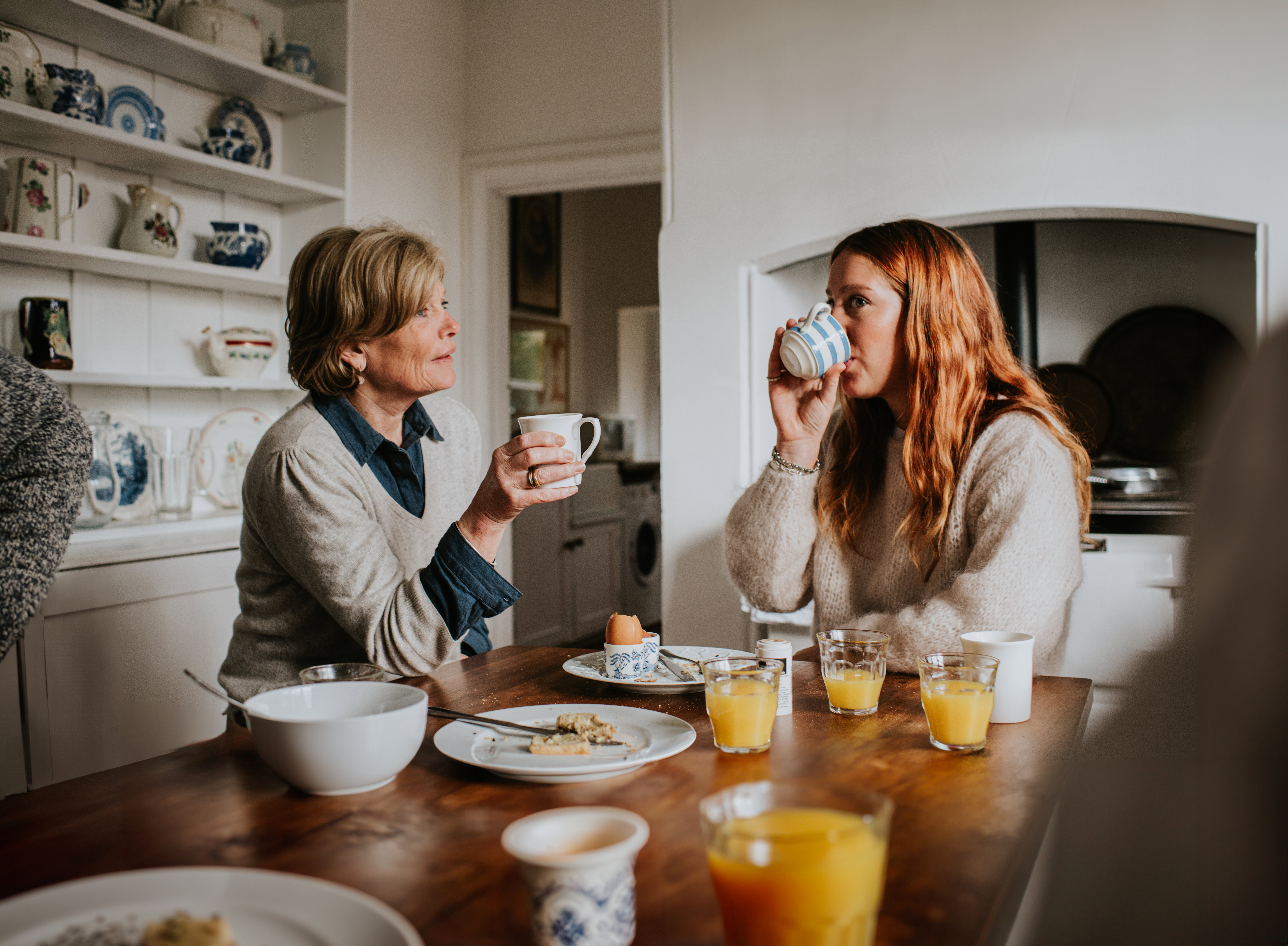 A mother and adult daughter drinking coffee in a stylish kitchen