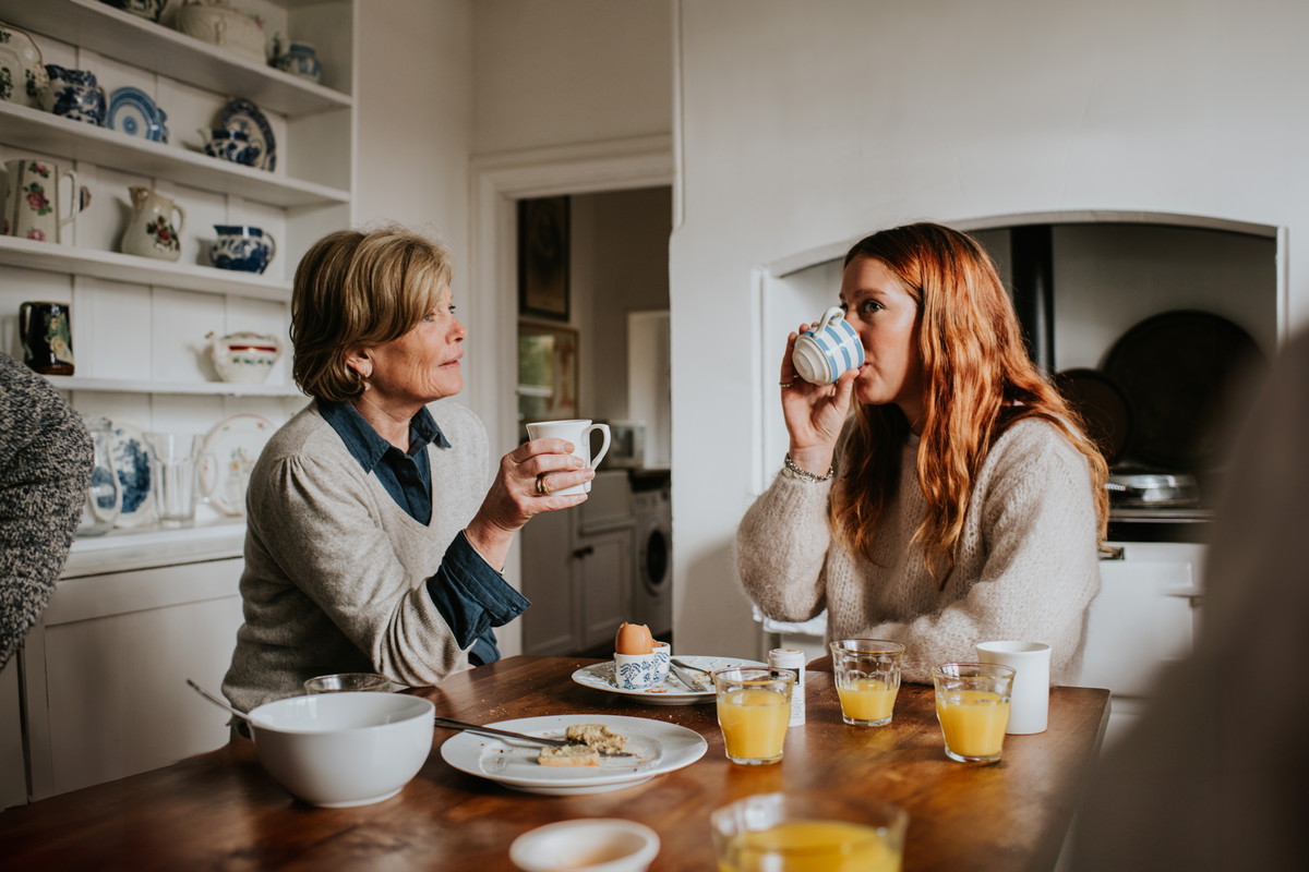 A mother and adult daughter drinking coffee in a stylish kitchen