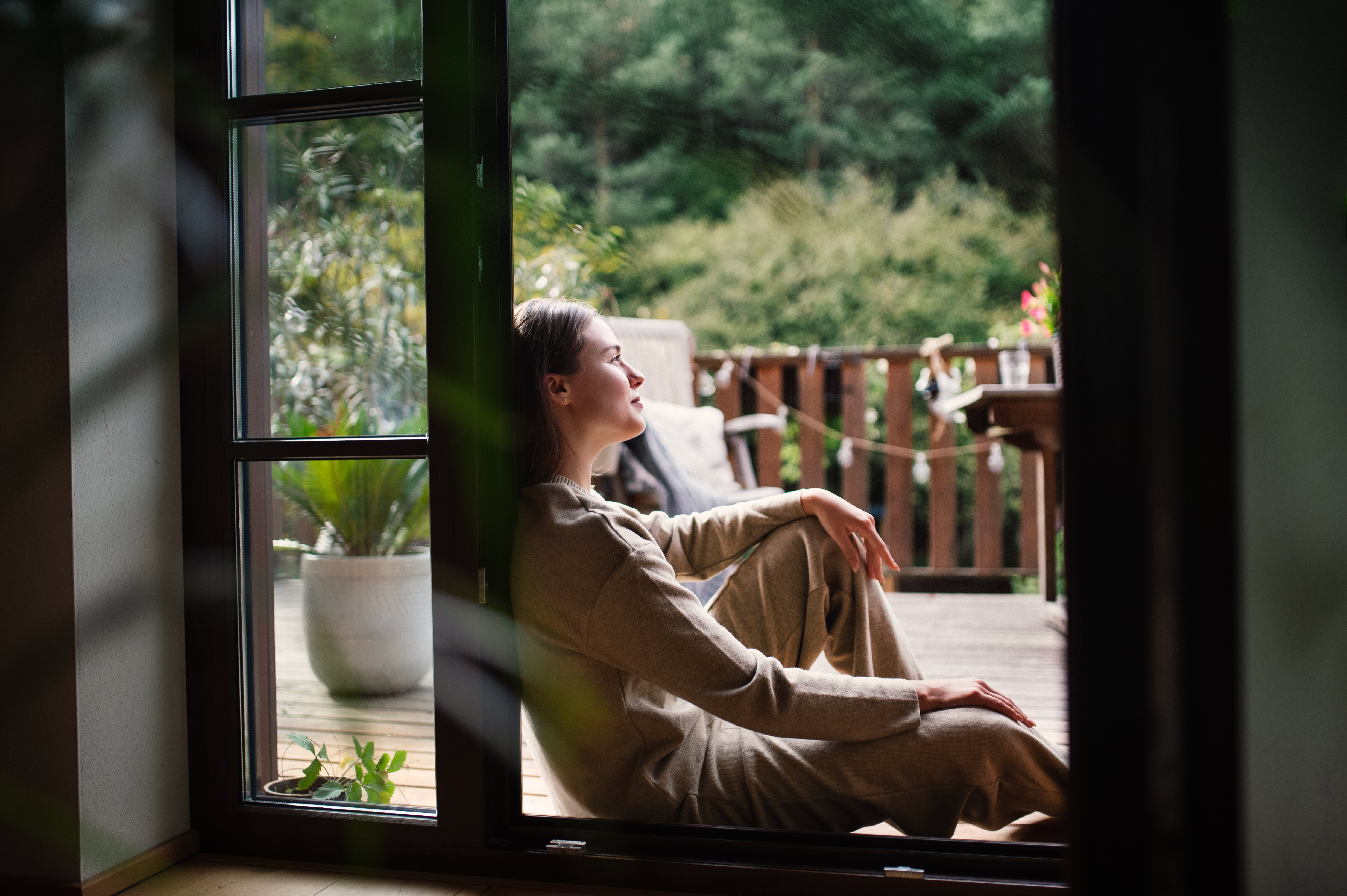 Woman resting in doorway of balcony doors, resting. Single woman enjoying free weekend. Concept of selfcare.