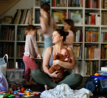 Capturing Maternal Burnout: Overwhelmed Mother Sitting on the Floor in the Living Room amidst Screaming Baby, Sibling Children's Activities, and Household Disorder