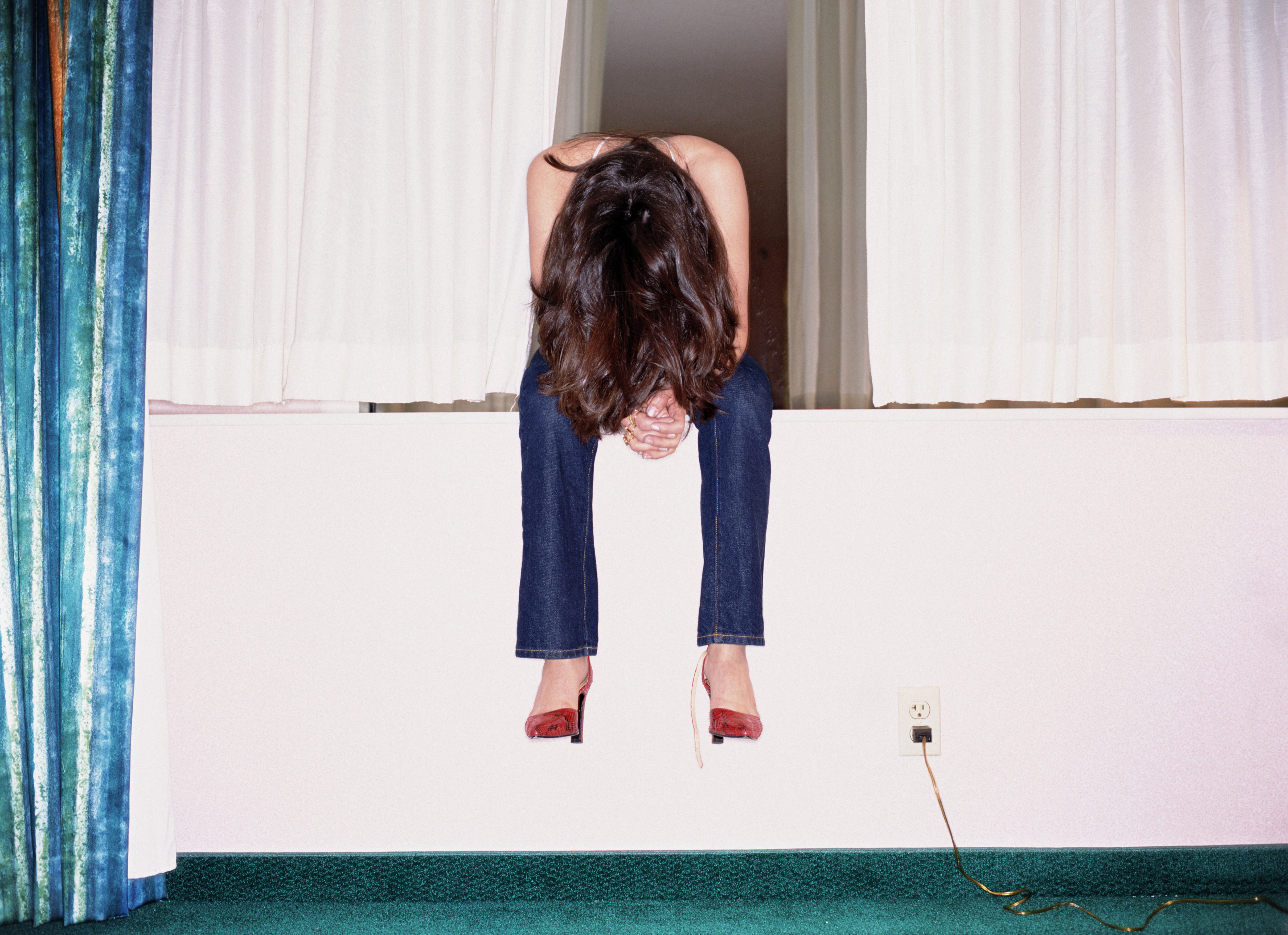 Woman sitting on hotel room windowsill, head bowed
