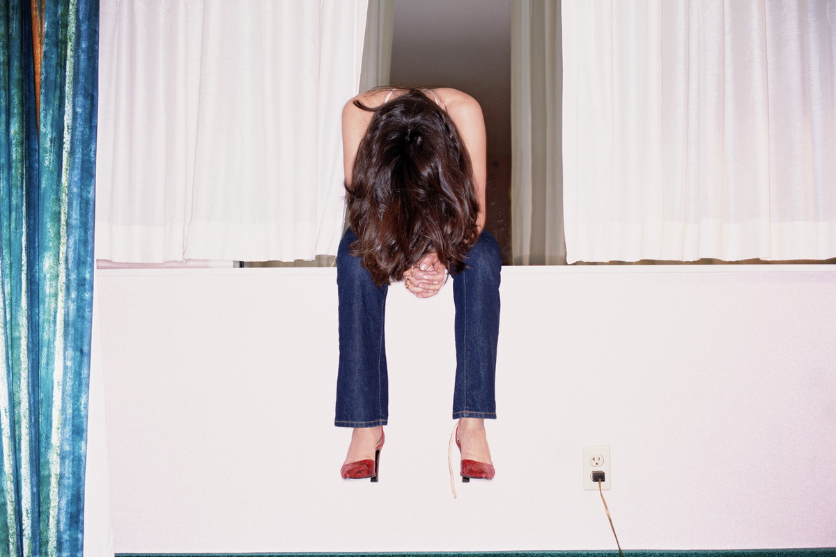 Woman sitting on hotel room windowsill, head bowed