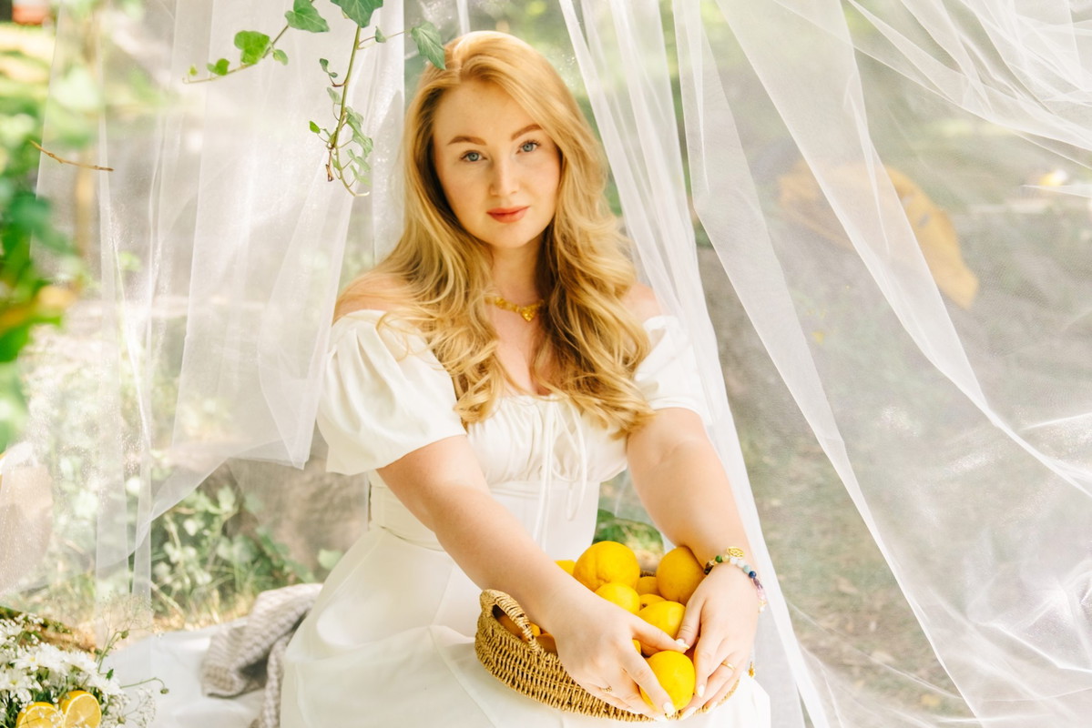 Romantic blonde woman with basket of lemons enjoying aesthetic outdoor picnic