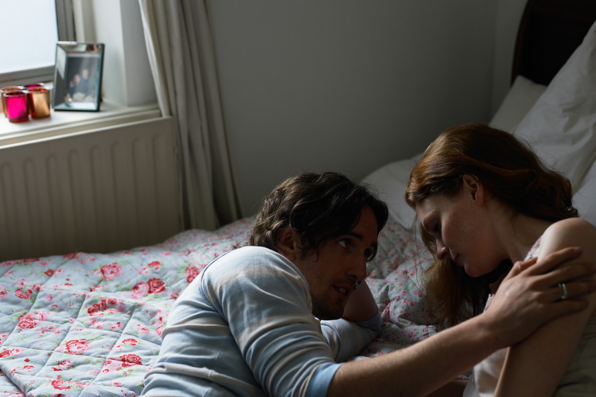 Couple lying on bed, man holding woman's shoulder
