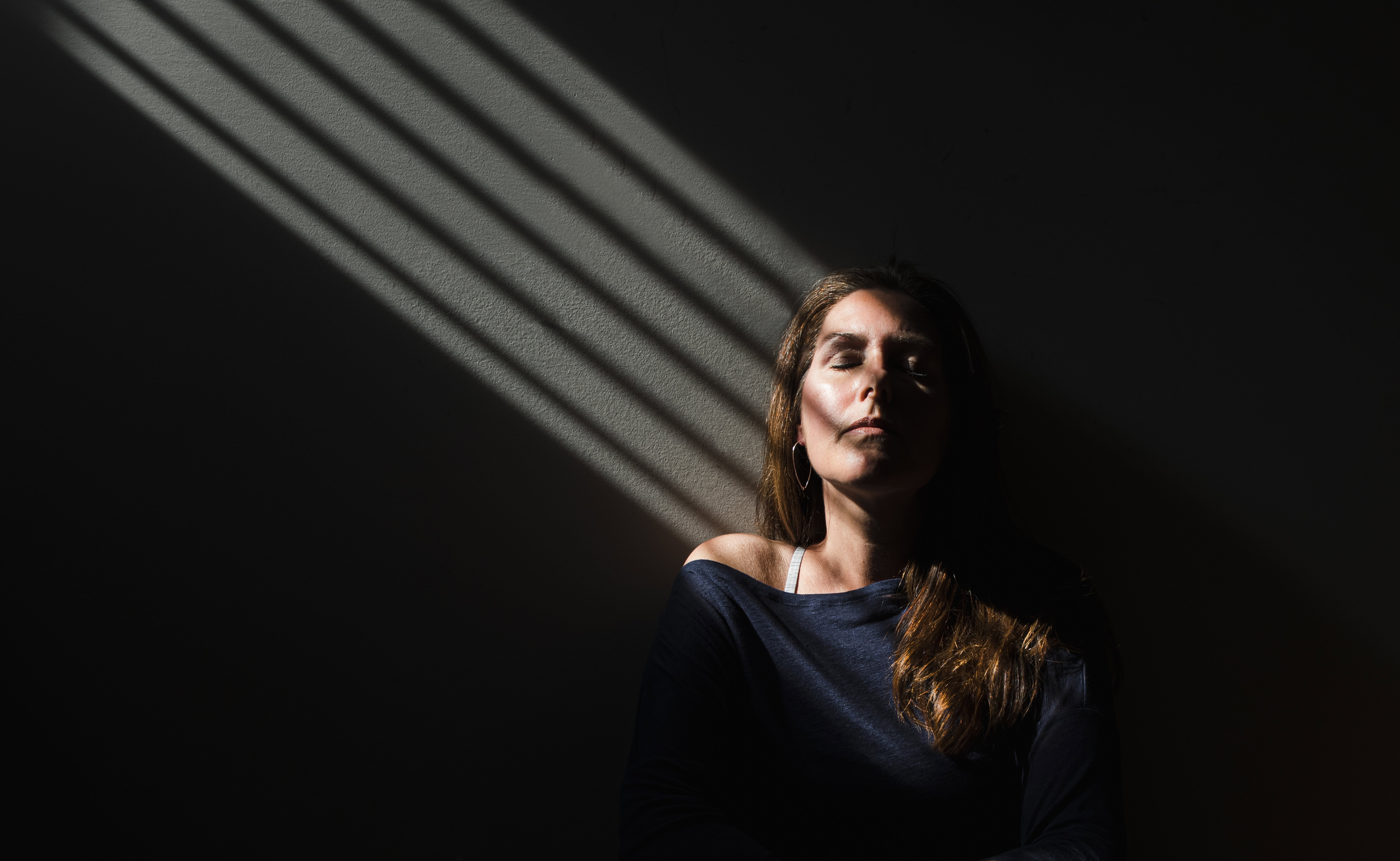 Portrait of a woman sitting in a patch of light with her eyes closed.