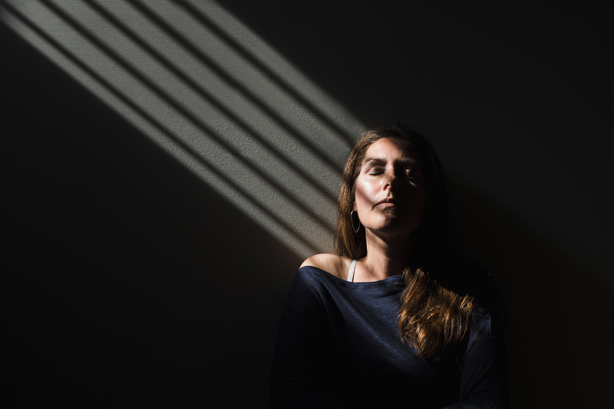 Portrait of a woman sitting in a patch of light with her eyes closed.