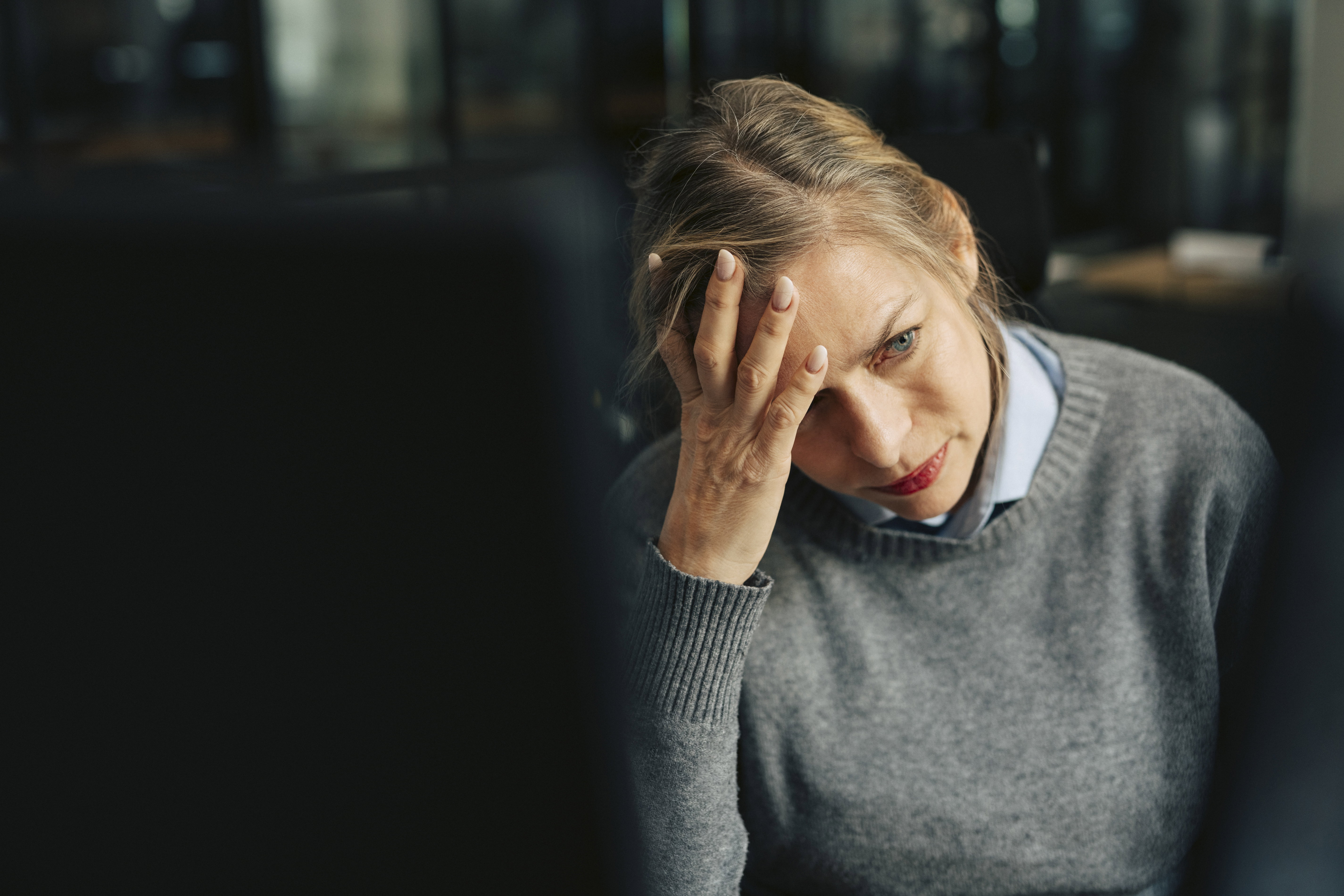 Depressed senior businesswoman with head in hand at office