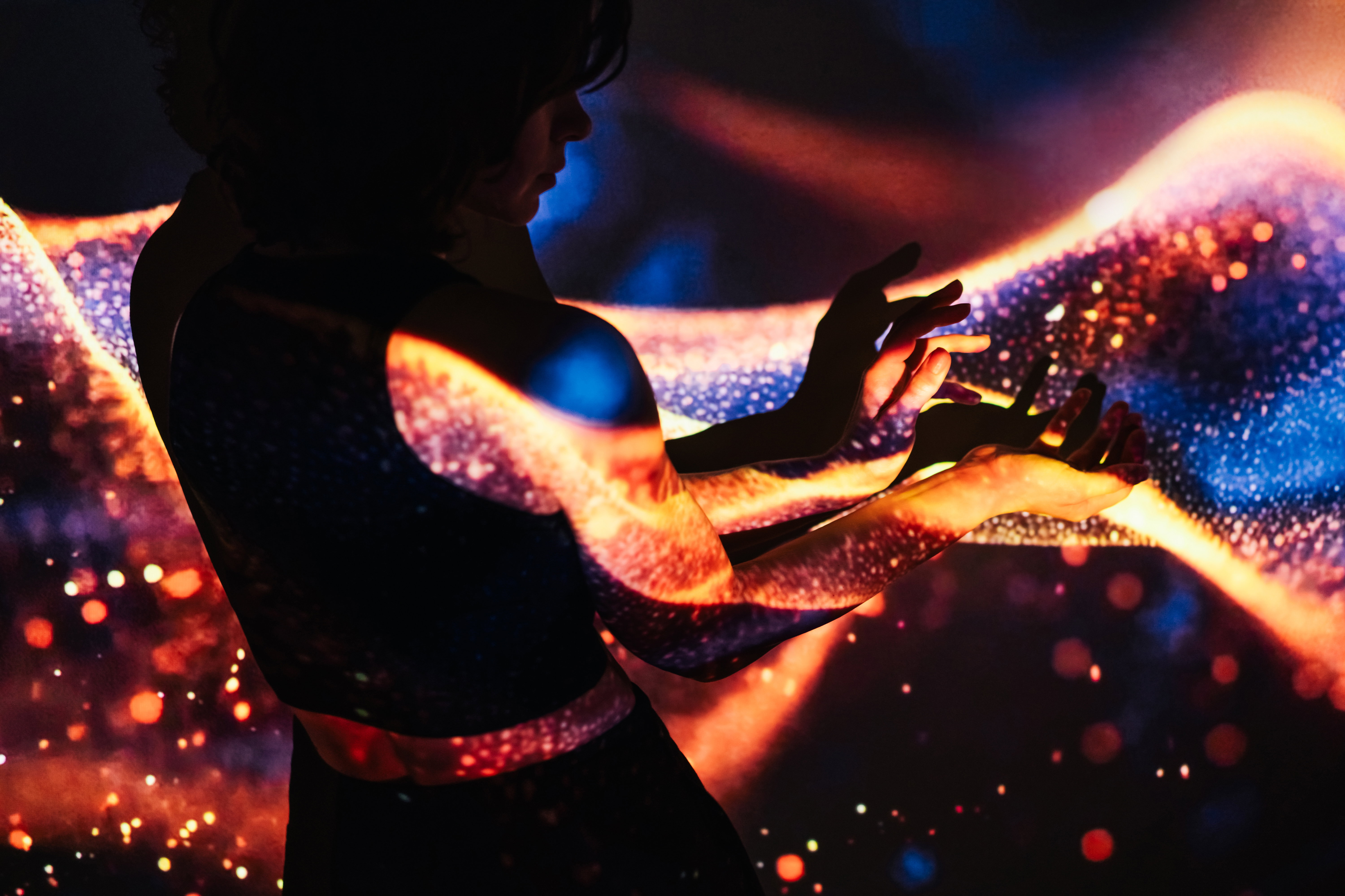 Woman’s hands in dark and projection of abstract light waves on them.