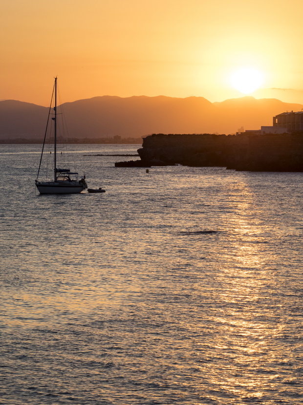 Silhouette of a sailboat in the sea near a harbor, during a sunset between the mountains on the island of Tabarca