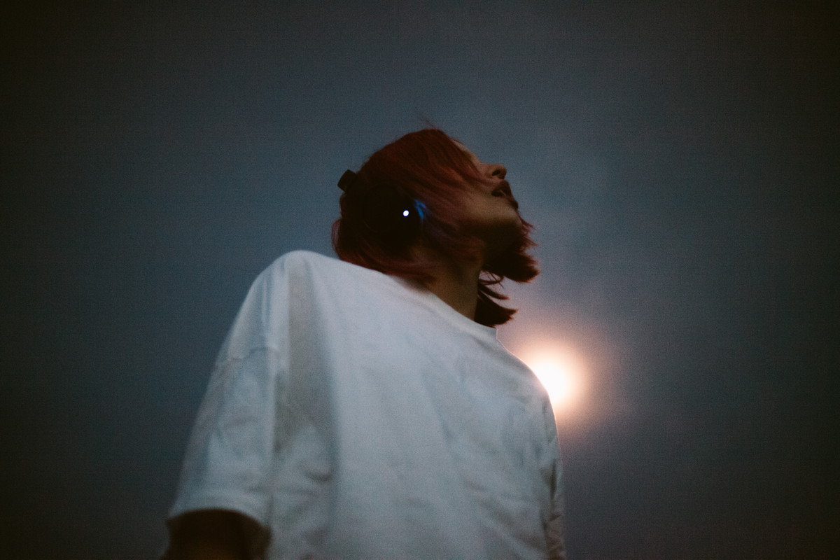 Young woman listening music in headphones standing against the sky at night