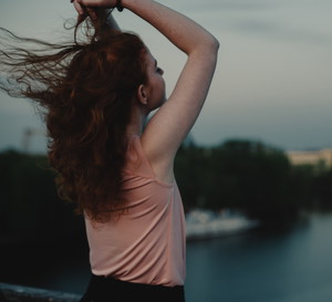 Rear view of woman with raised arms standing on bridge at dusk