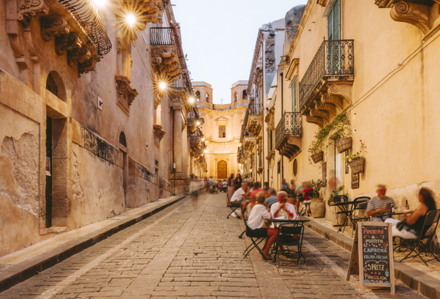 People dining outside restaurants and bars at dusk in Noto