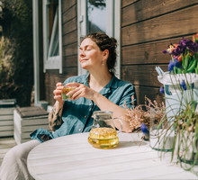 Woman relaxing with herbal tea on porch of wooden cottage