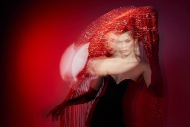 Elegant woman in a black dress under red light with veil and dramatic double exposure