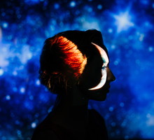 A striking profile portrait of a woman silhouetted against a deep blue starry night sky, with a crescent moon projected onto her face.